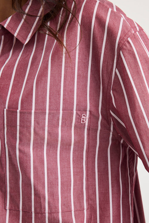 Woman wearing an oversized burgundy and white vertical stripe button-up shirt made from 100% cotton, styled with blue jeans.