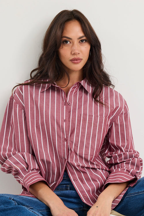 Woman wearing an oversized burgundy and white vertical stripe button-up shirt made from 100% cotton, styled with blue jeans.