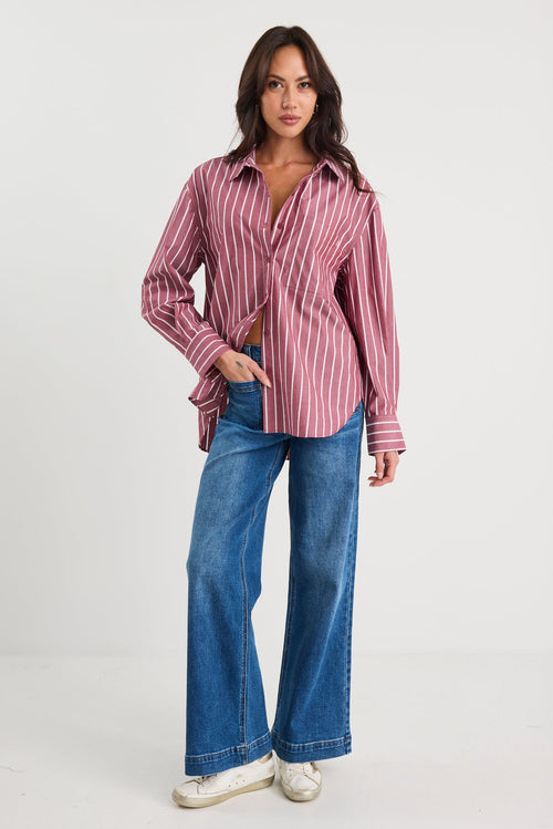 Woman wearing an oversized burgundy and white vertical stripe button-up shirt made from 100% cotton, styled with blue jeans.