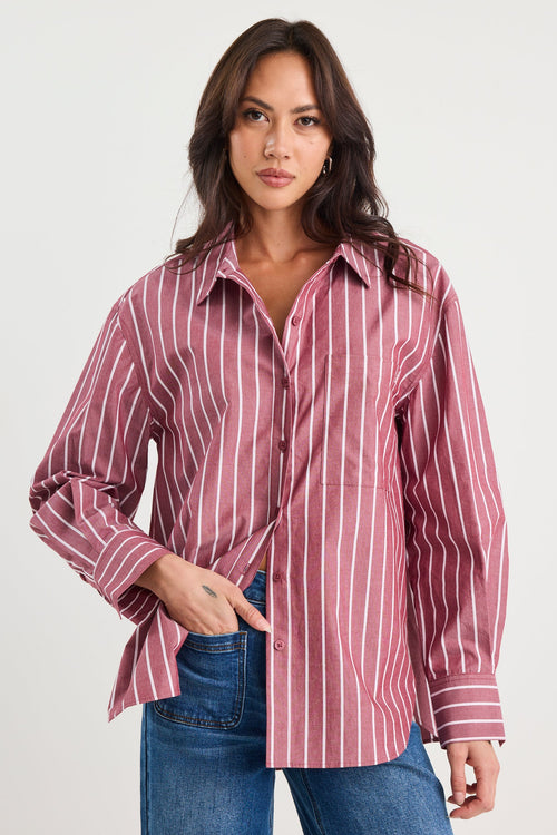 Woman wearing an oversized burgundy and white vertical stripe button-up shirt made from 100% cotton, styled with blue jeans.