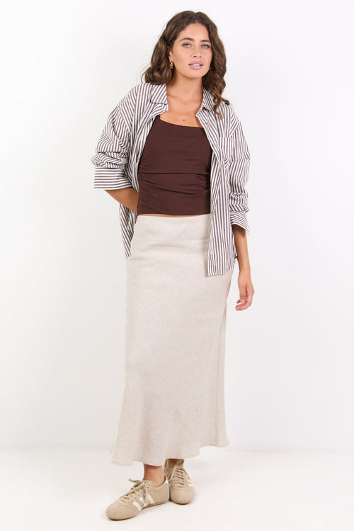 Woman wearing a plaid shirt, brown top, and beige skirt on a white background