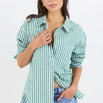 Woman wearing a green and white striped shirt with rolled-up sleeves and light blue jeans on a white background