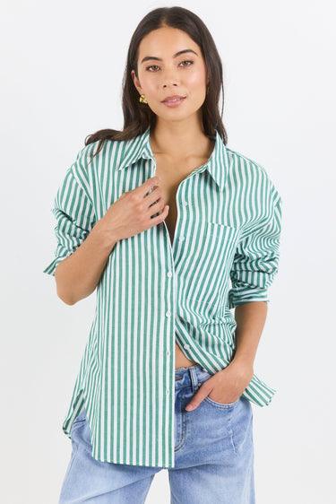 Woman wearing a green and white striped shirt with rolled-up sleeves and light blue jeans on a white background