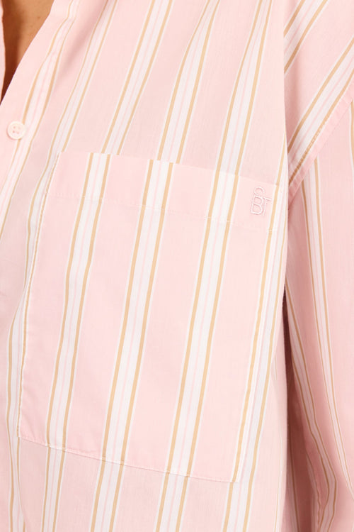 Close-up of a pink button-up shirt with vertical white and thin gold stripes, featuring a chest pocket and a small embroidered logo on the pocket.