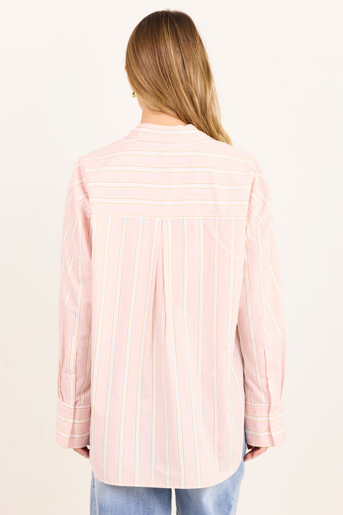A woman viewed from the back wearing a light pink long-sleeve button-up shirt with thin white vertical stripes and light blue jeans, set against a plain off-white background.