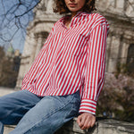 Woman in a red and white striped shirt and blue jeans sitting in front of a cathedral.