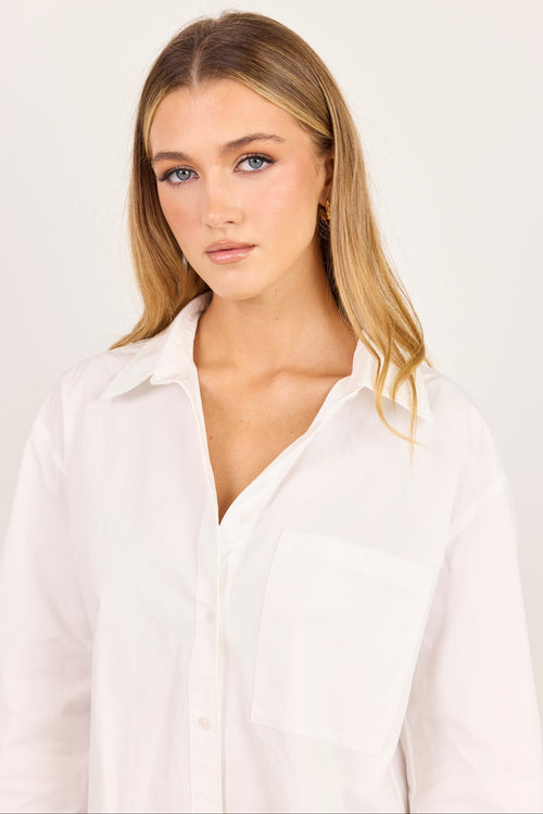 A woman with blonde hair wearing a white button-down shirt, photographed against a plain light background.