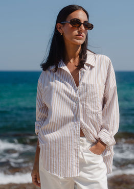Woman in a striped shirt and sunglasses standing on a beach with ocean in the background