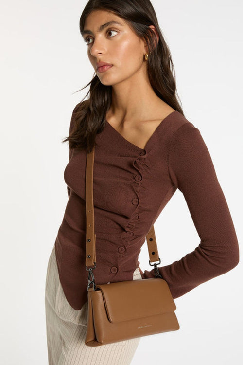 A structured camel-brown leather shoulder bag with a rectangular flap-over design and fine pebble texture. It features a detachable wide strap with black metal hardware and 