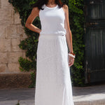 Woman in a white dress standing outdoors against a stone wall and greenery.