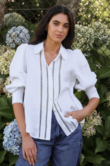 Woman wearing a white blouse with black trim in front of hydrangea flowers