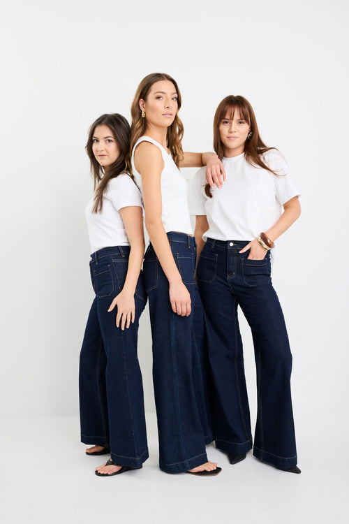 Three women wearing white tops and dark blue jeans standing against a white background