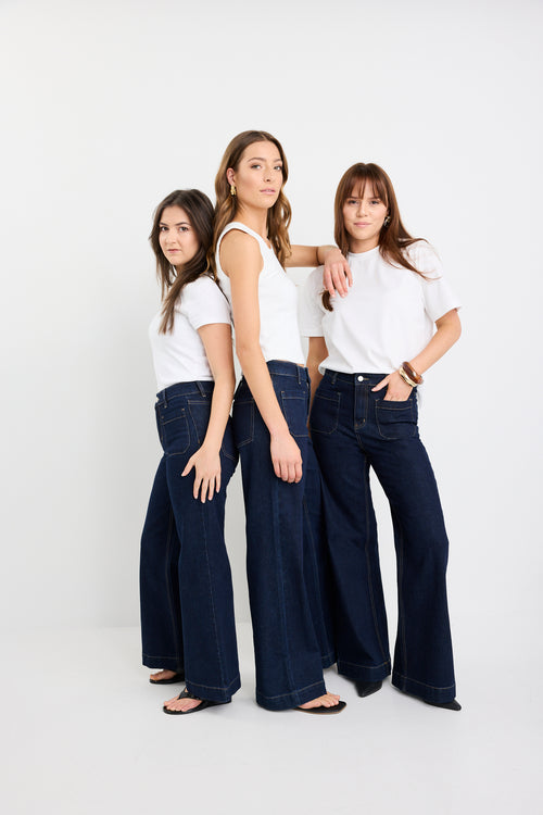 Three women wearing white tops and dark blue jeans standing against a white background