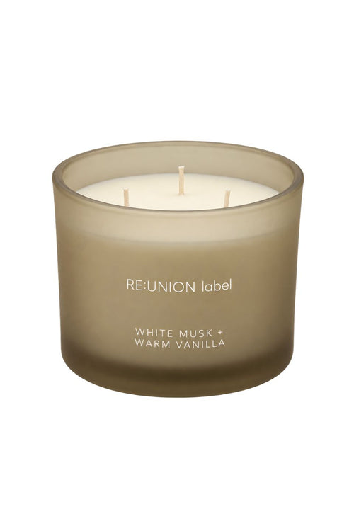 A three-wick scented candle in a frosted taupe-brown glass jar with white wax, labeled 'RE:UNION label' and 'WHITE MUSK + WARM VANILLA' on a plain white background.