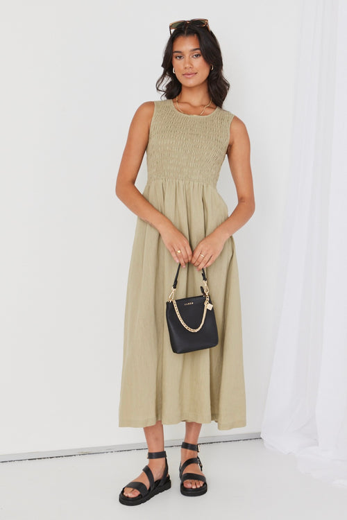 model posing in light green midi dress and black sandals holding a black bag