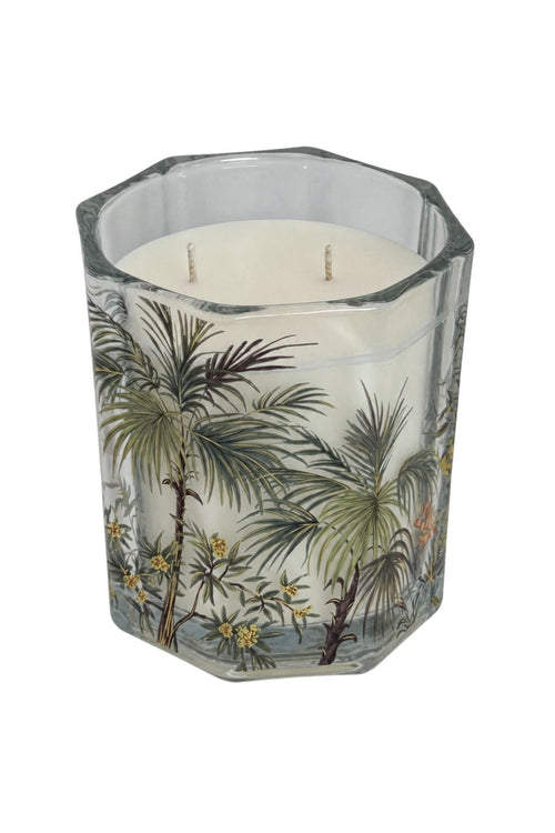 A white wax candle in a clear octagonal glass container decorated with a vintage-style tropical palm tree illustration, shown against a plain white background.