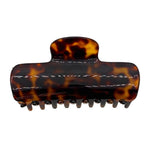 A classic hair claw clip in a glossy tortoiseshell pattern, featuring dark brown and amber-orange mottled tones with white contrast stitching, shown against a plain white background.