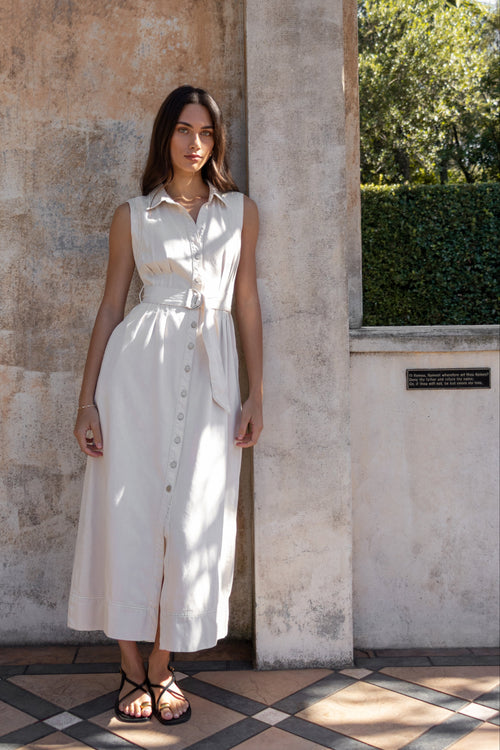 Woman in a white dress standing against a textured wall with greenery in the background