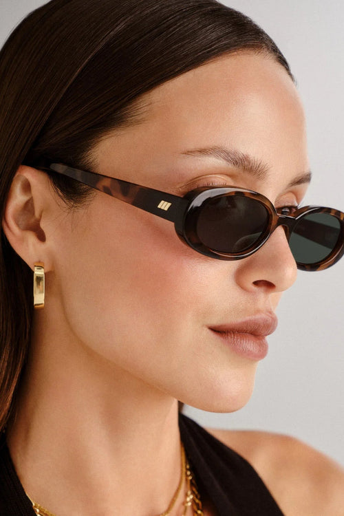 Woman wearing tortoiseshell sunglasses with a neutral background