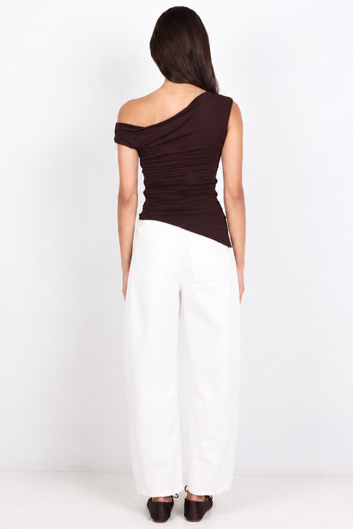 A woman viewed from behind wearing a dark brown off-the-shoulder ruched top and white wide-leg pants, standing against a plain white studio background.
