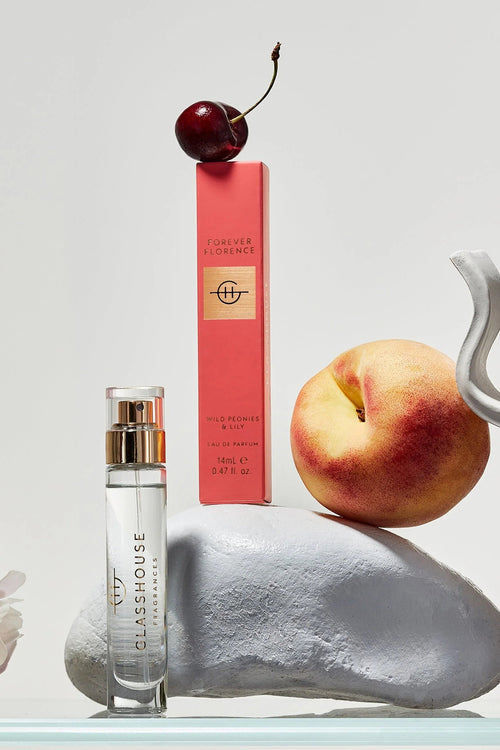 Perfume bottle, cherry, peach, and white flower on a light gray background