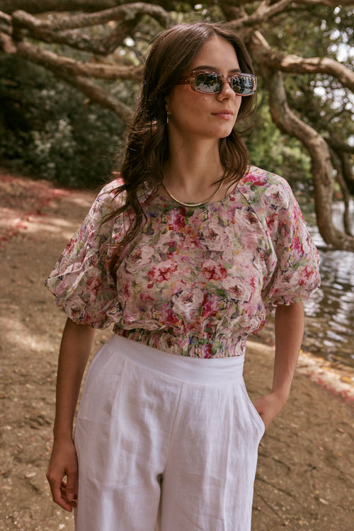 model poses on beach with floral red top and white pants