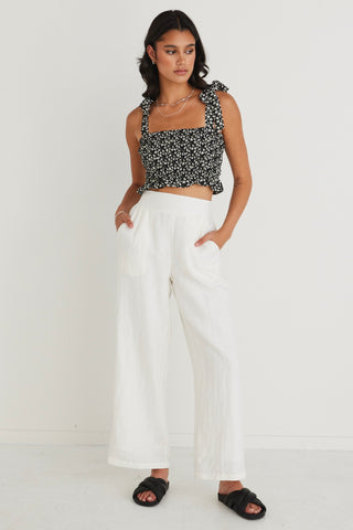 model in black floral cami top and white pants with black slides