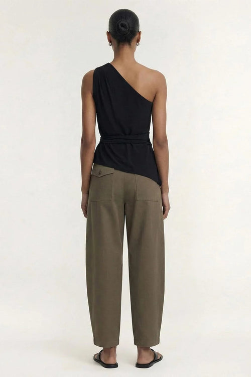 A model viewed from the back wearing a black one-shoulder wrap top and olive green wide-leg trousers, paired with black sandals, against a plain off-white studio background.