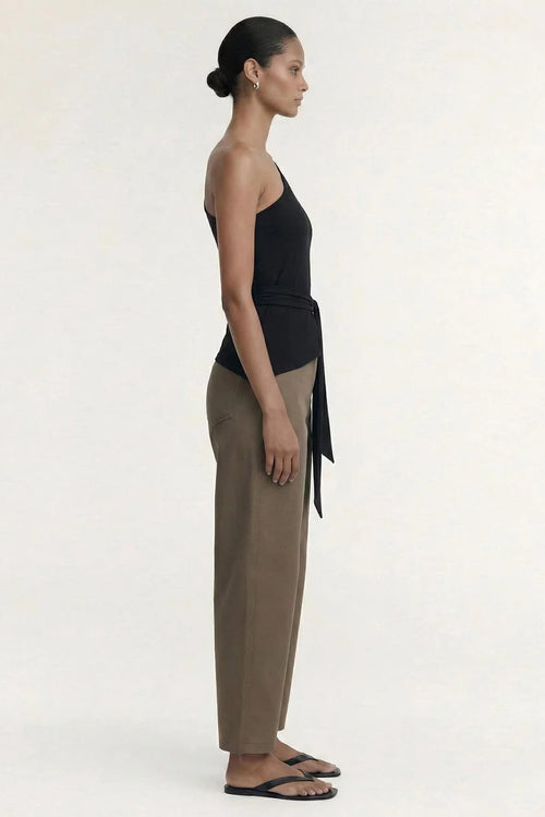 A model shown in profile wearing a black halter top with a side tie, beige wide-leg trousers, and black flip-flops against a plain off-white studio background.