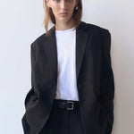 Person wearing a black suit and white shirt against a plain background