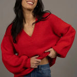 Woman wearing a red sweater and blue jeans against a gray background