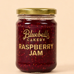 Bluebells Cakery Raspberry Jam in a glass jar with gold lid.