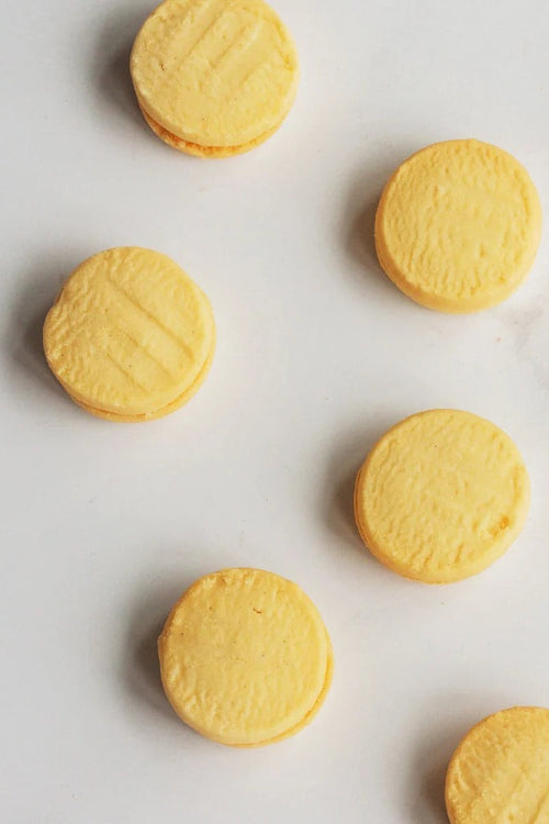 Several round pale yellow melting moments arranged on a light white marble surface.