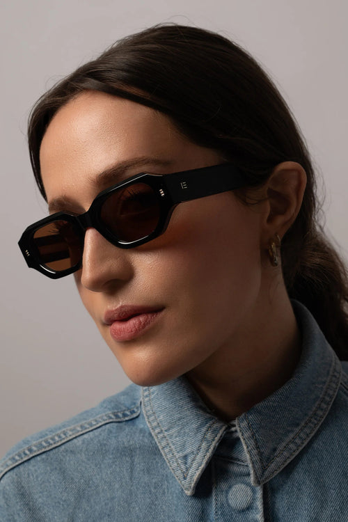 Woman wearing black sunglasses and a denim jacket against a gray background