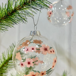 Clear glass ornament with floral design hanging on a Christmas tree branch.