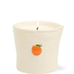 A lit cream-colored ceramic candle holder with a small orange and green leaf illustration on the front, set against a plain white background.