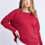 Woman wearing a red sweater over a white shirt with gray pants on a light gray background