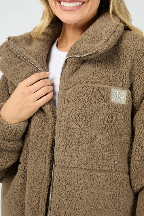 Person wearing a brown fleece jacket with a brand logo on a white background