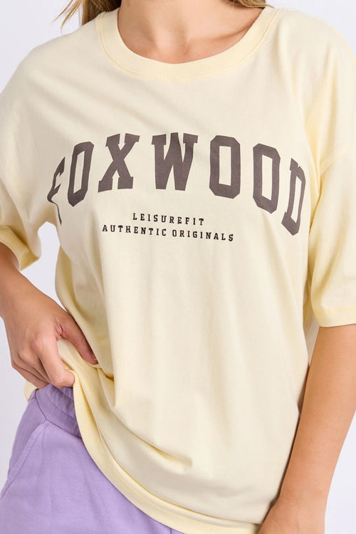 Person wearing a light yellow t-shirt with 'Foxwood' branding on a plain background