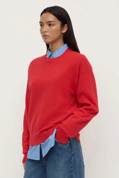 Person wearing a red sweater, light blue shirt, and blue jeans on a white background