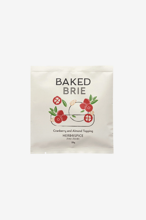 A single packet of Baked Brie Cranberry and Almond Topping, Herb & Spice, shown on a clean white background. The packaging is a cream-colored stand-up pouch with a graphic of a brie cheese wheel topped with red cranberries and green leaves.