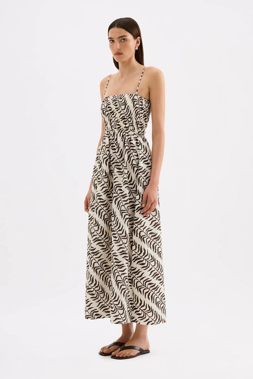 A woman modeling a sleeveless maxi dress with a black and off-white wavy abstract pattern, standing against a plain white studio background.