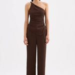 A woman modeling a dark brown one-shoulder wrap-style jumpsuit with matching wide-leg pants, photographed against a clean white studio background.
