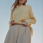 Woman wearing a yellow sweater and beige pants against a clear blue sky.
