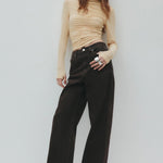 Woman wearing a beige top and black pants against a white background