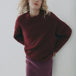 Woman wearing a burgundy sweater and skirt against a white background