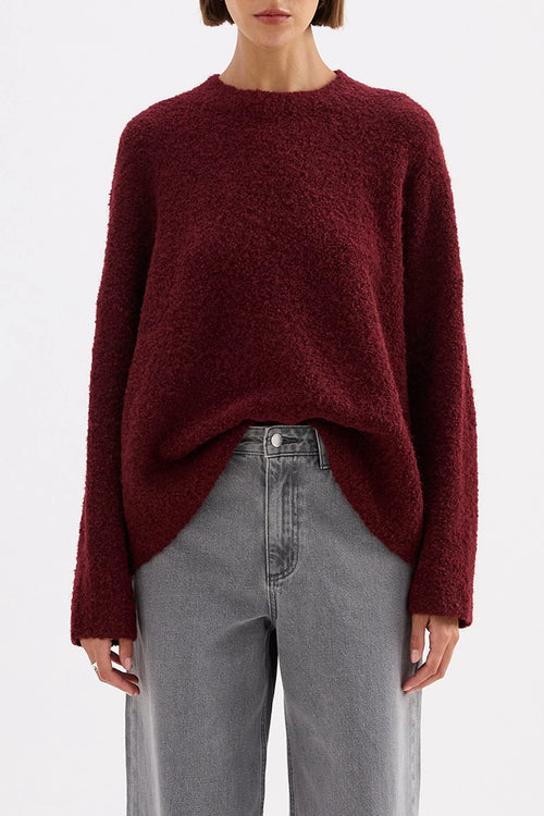 Person wearing a burgundy sweater and gray pants on a white background