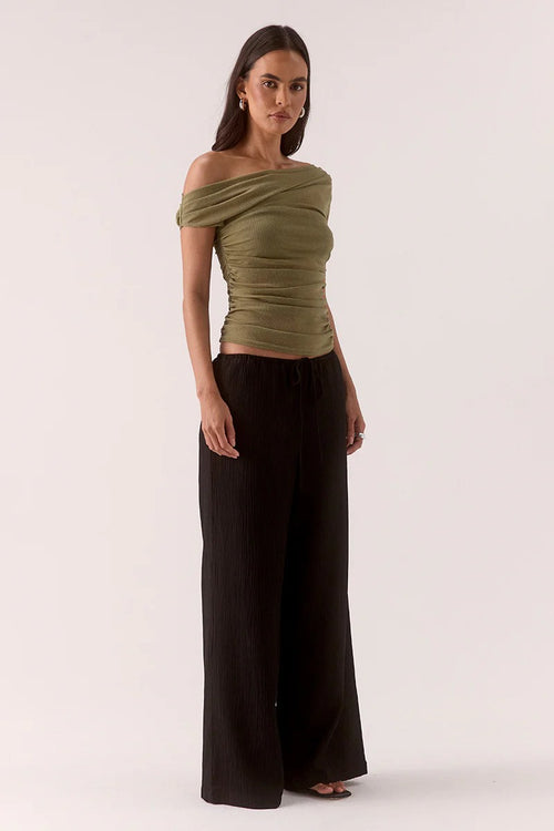 Woman wears a green ruched top and black pants