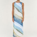 A woman modeling a sleeveless, high-neck maxi dress with an abstract, fluid wave pattern in shades of blue, beige, and white, set against a plain light background.