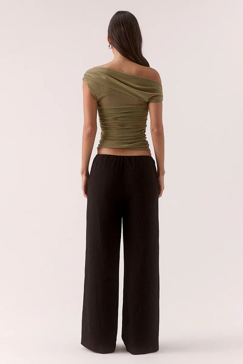 Woman wears a green ruched top and black pants